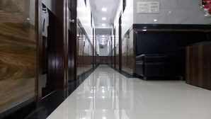 A long, narrow hallway with a polished floor, wooden paneling on the walls, and a seating area with a dark-colored sofa. - Hotel Sion Residency (Mumbai)
