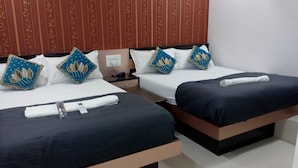Habitación de hotel con dos camas, cada una con cubrecama azul oscuro, almohadas blancas y almohadas decorativas azules con diseño de hojas. Hay un control remoto en la cama de la izquierda y una toalla doblada con cuidado en la de la derecha.
