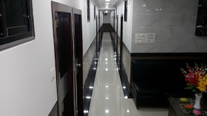 Un pasillo de hotel moderno con piso brillante, puertas de madera oscura y una pared de mármol.