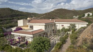 A two-story building with a tiled roof, surrounded by greenery and hills. - Argentiera Inn (Sassari)