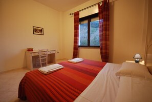 A bedroom with a bed, a desk, and a window with curtains. - Argentiera Inn (Sassari)