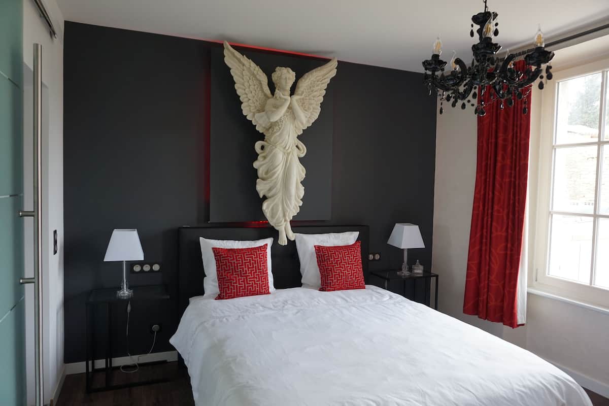 Een hotelkamer met een groot bed, twee nachtkastjes, een kroonluchter en een aan de muur bevestigde engelbeeld.