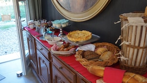 Une table de buffet garnie de divers aliments, notamment des pâtisseries et du pain, placée devant un mur sombre orné d’un grand tableau encadré.