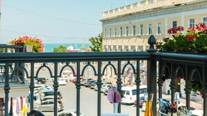 Un balcón con una mesa dispuesta para el desayuno, con vistas a una calle con coches estacionados y un edificio al fondo.
