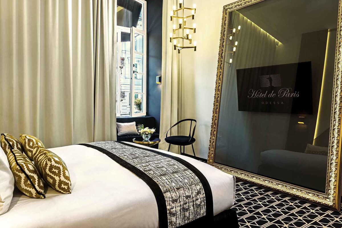 A hotel room with a large bed, a mirror, a sofa, and a window with curtains.