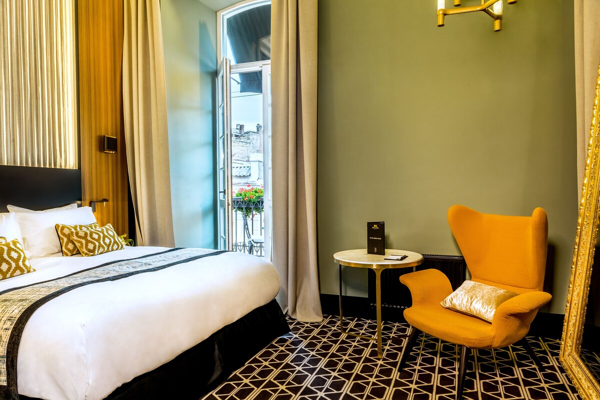 Habitació d'hotel amb un llit, una cadira, una taula petita i vista a l'exterior.