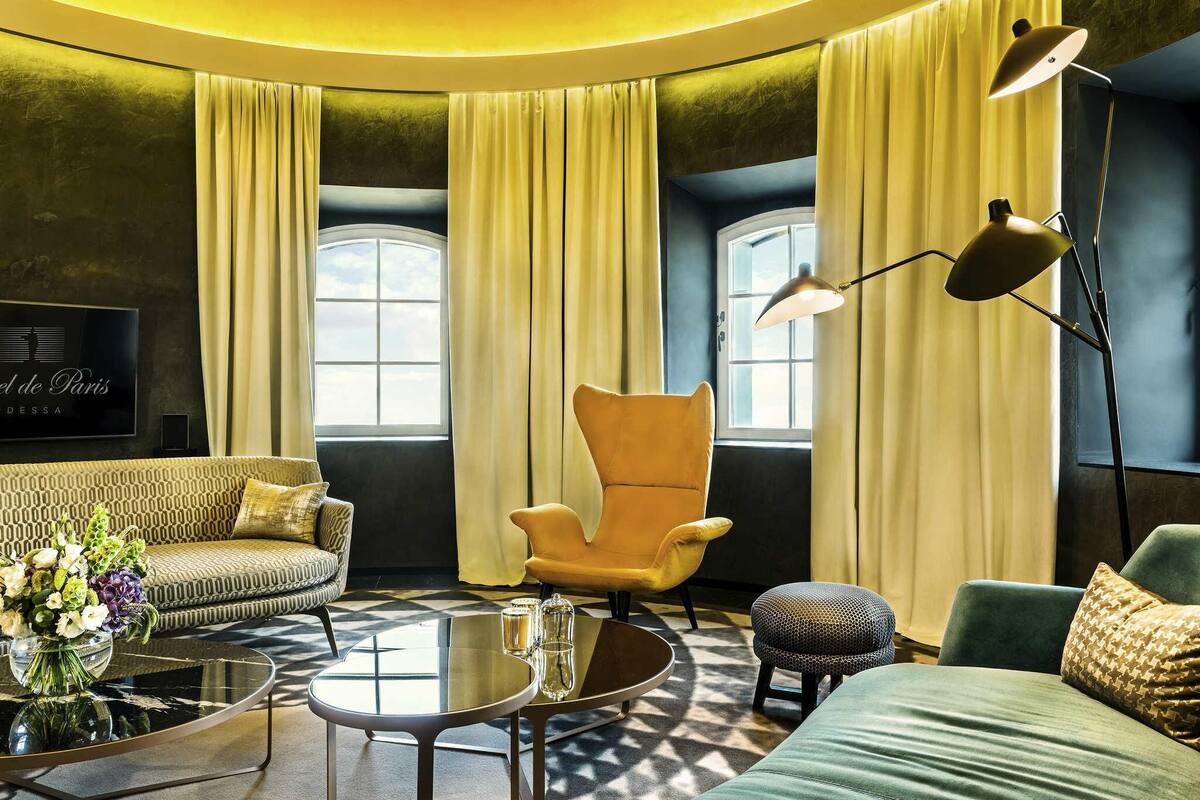 Una sala de estar moderna con un sofá, un sillón, un reposapiés, una mesa de centro de vidrio y una lámpara de pie.
