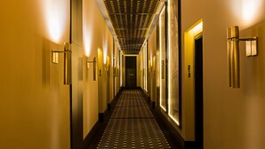 A hotel hallway with a patterned floor, wall-mounted light fixtures, and doors with numbers. - Hotel de Paris Odesa - MGallery (Odesa)