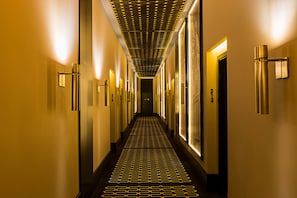 A hotel hallway with a patterned floor, wall-mounted light fixtures, and doors with numbers. - Hotel de Paris Odesa - MGallery (Odesa)