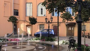 Un patio con una fuente, un coche azul y un edificio con ventanas de arco.