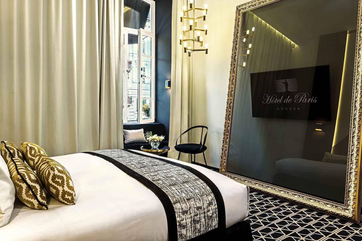 Una habitación de hotel con una cama grande, un espejo, un sofá y una ventana con cortinas.