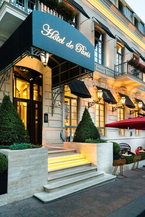 Das Hotel de Paris mit einer markanten Fassade, Stufen zum Eingang und einer Außenbereichsitzgelegenheit.