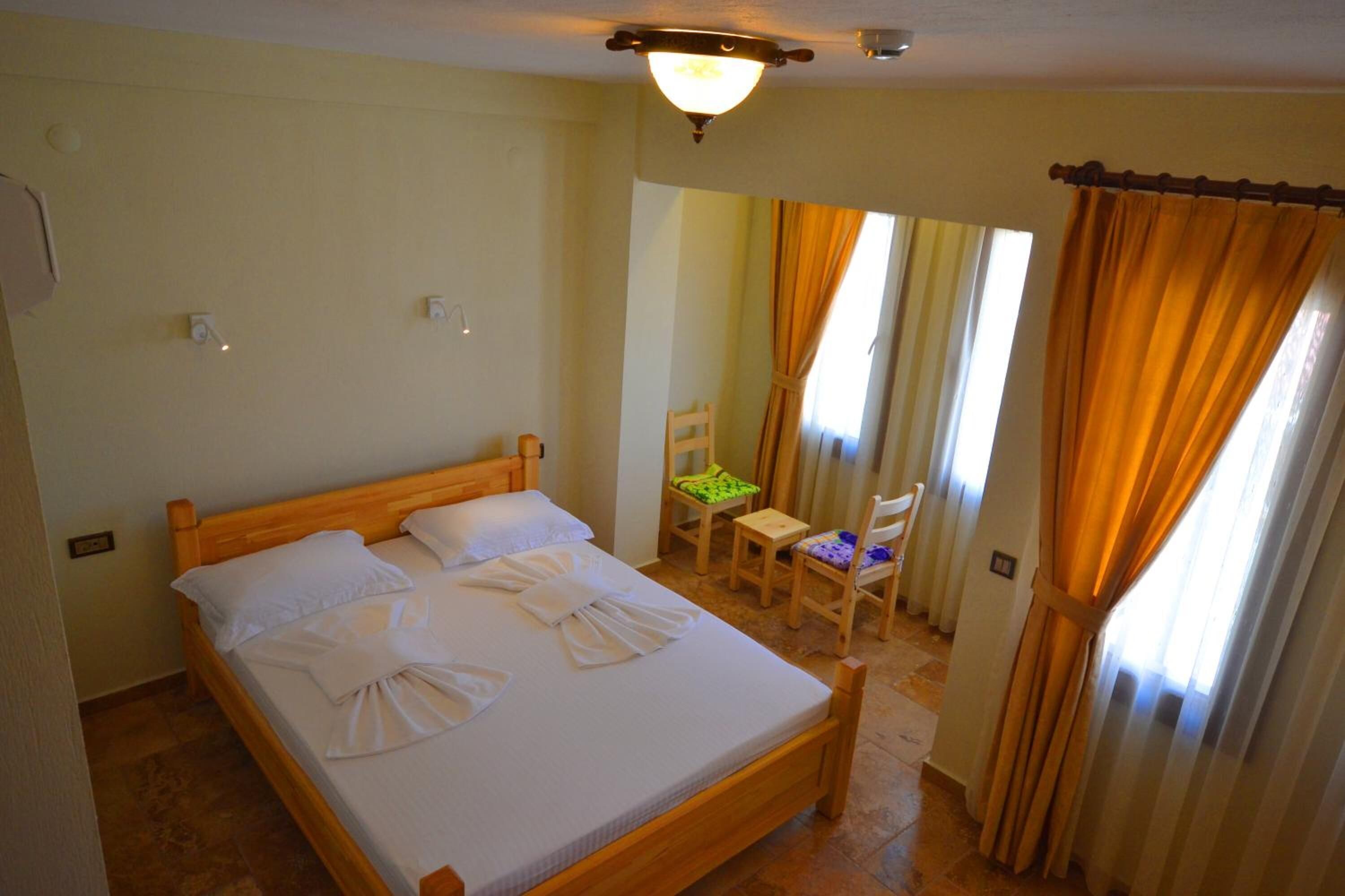 Una cama bien hecha con ropa blanca y toallas, un cabecero de madera y una pequeña mesa con sillas en la habitación contigua.