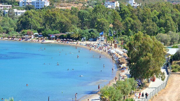 A coastal beach with clear blue water, a sandy shore, and buildings in the background. - Doada Hotel (Datça)