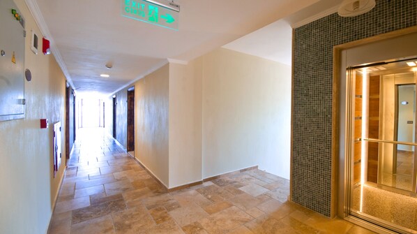 A hotel corridor with a tiled floor, an exit sign, and a door with a metal mesh grille.