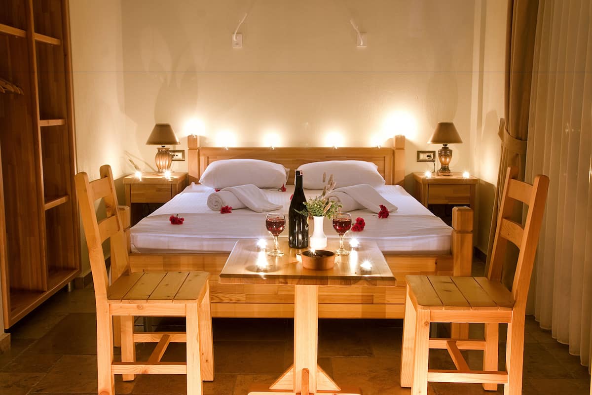 A neatly made bed with white linens, a bottle of wine, and two glasses on a wooden table in a hotel room.