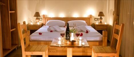 A neatly made bed with white linens, a bottle of wine, and two glasses on a wooden table in a hotel room.