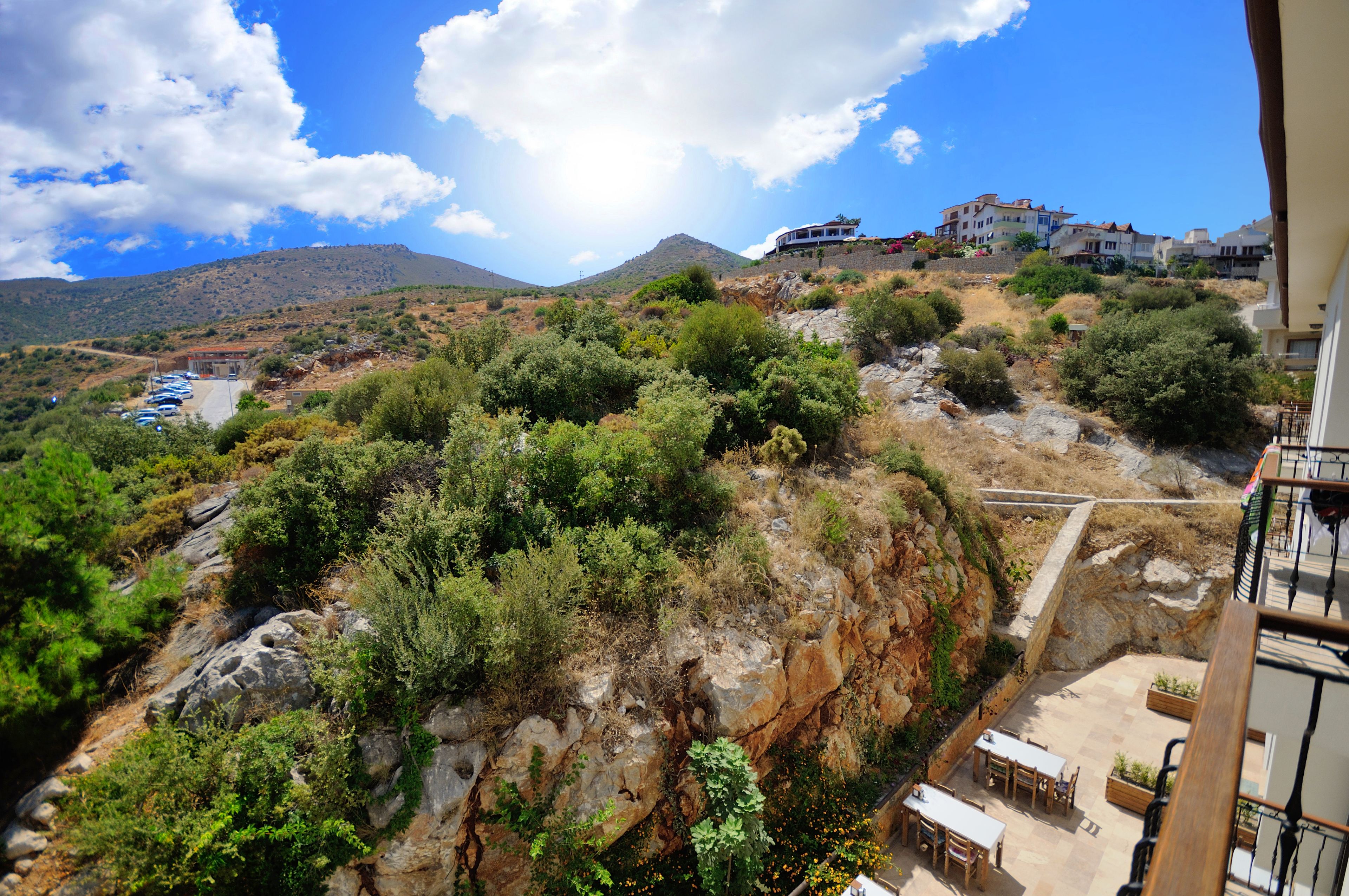 Une vue sur une colline, avec un bâtiment au sommet, un espace de stationnement et un balcon agrémenté de mobilier d’extérieur.