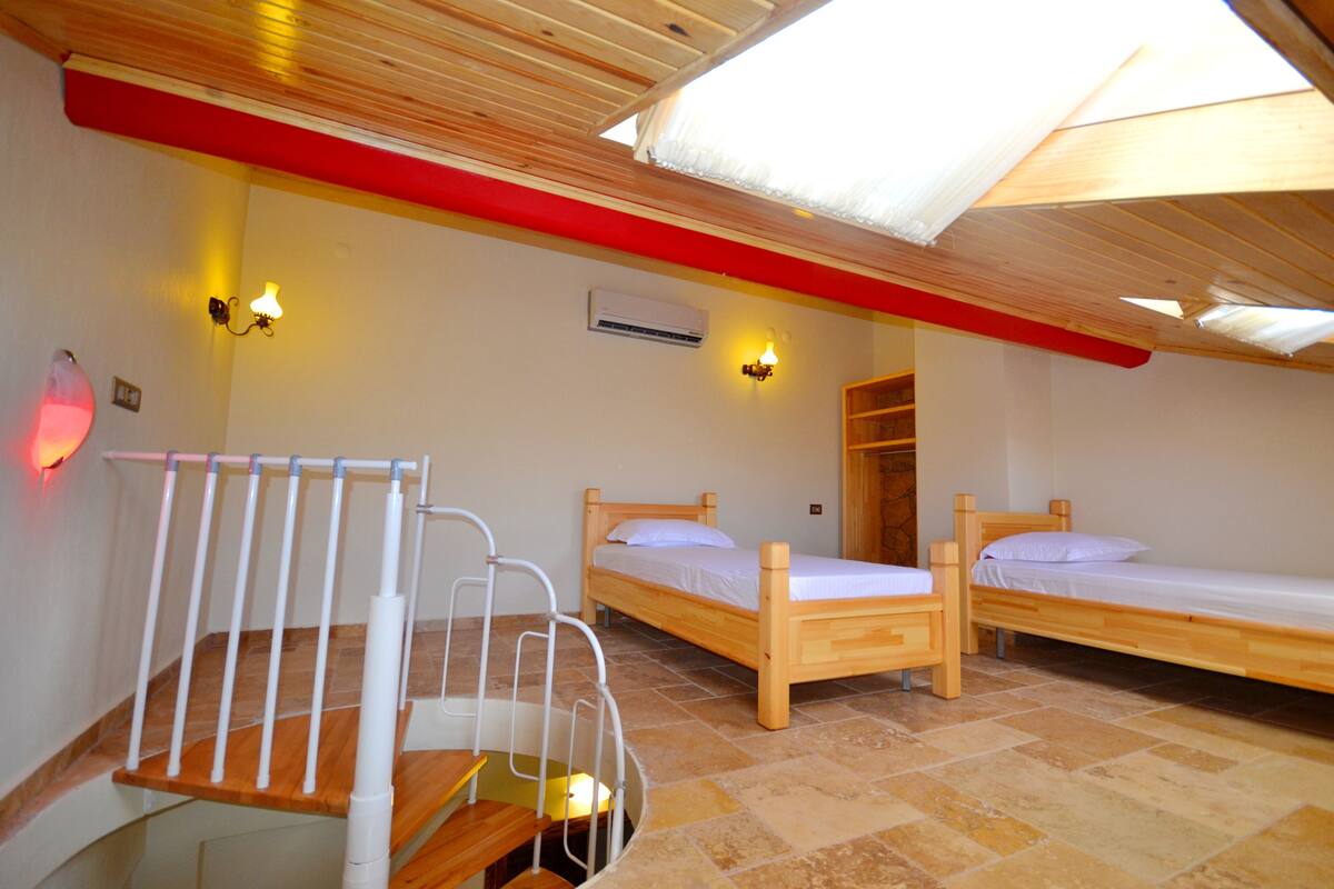 A room with two wooden beds, a wooden bench, a white chair, and a red beam on the ceiling.