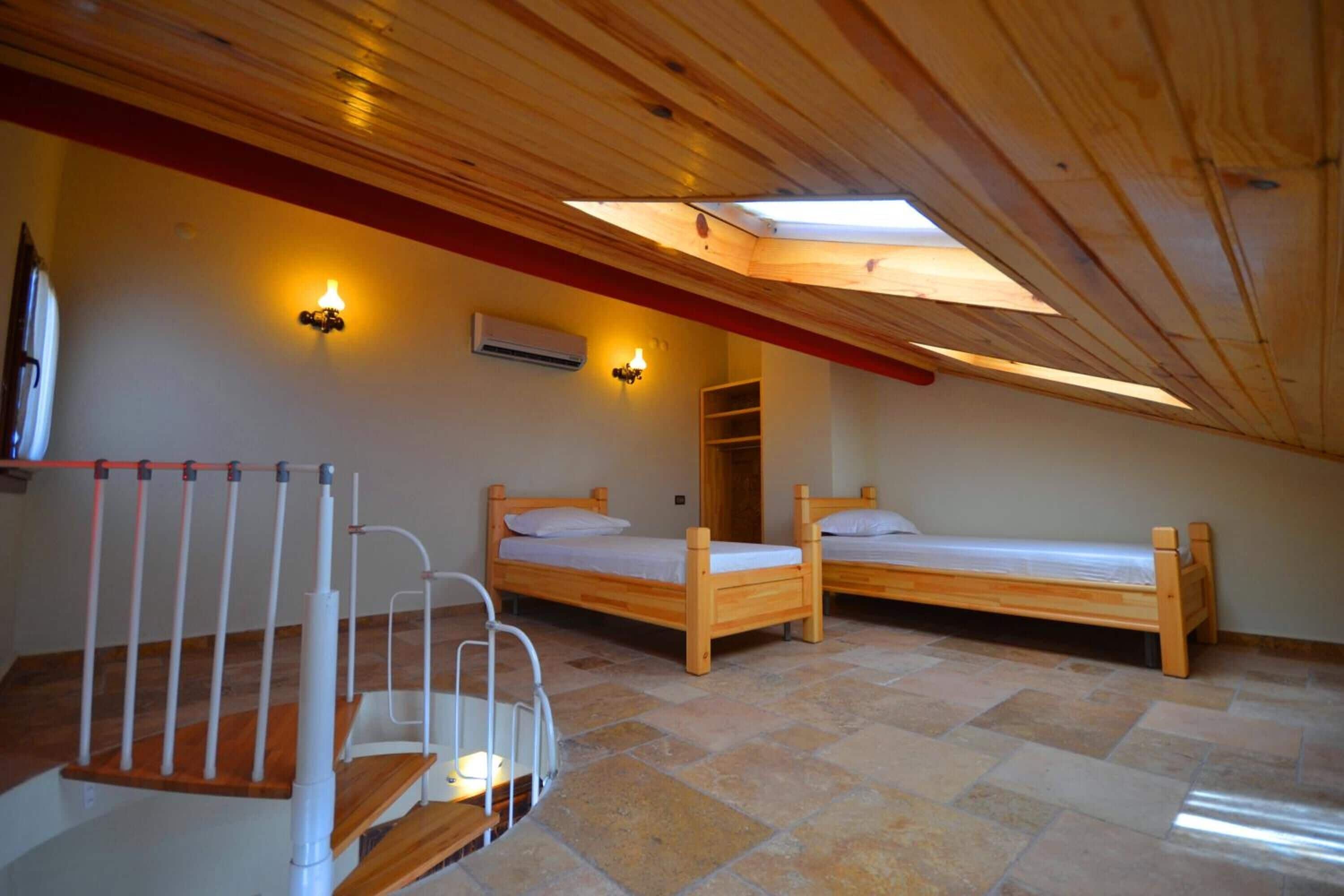 A room with two wooden beds, a white crib, a skylight, and a red beam on the ceiling.