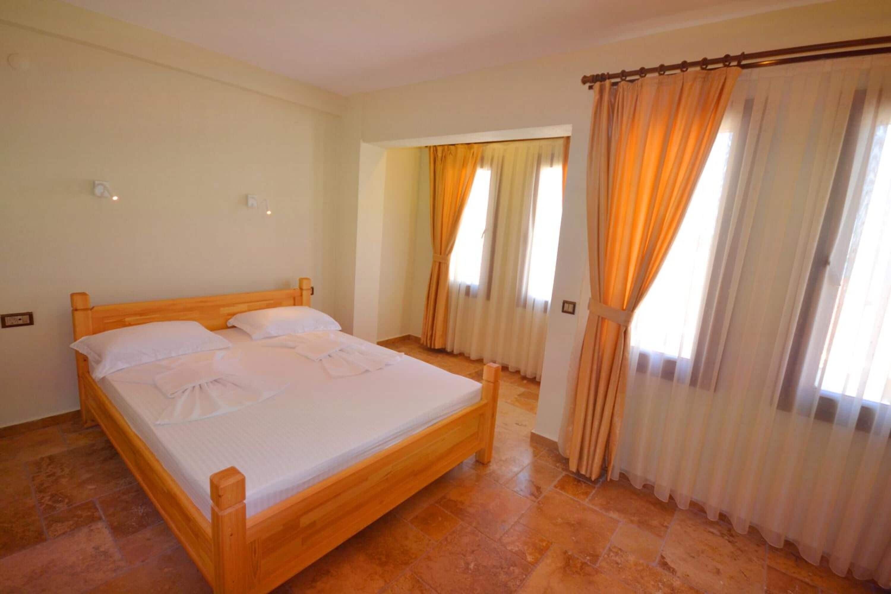 Un dormitorio con cama de madera, ropa de cama blanca y cortinas.
