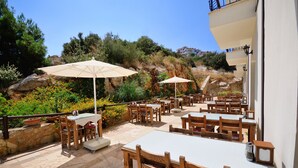 An outdoor patio with tables and chairs, surrounded by greenery and a rocky hillside. - Doada Hotel (Datça)