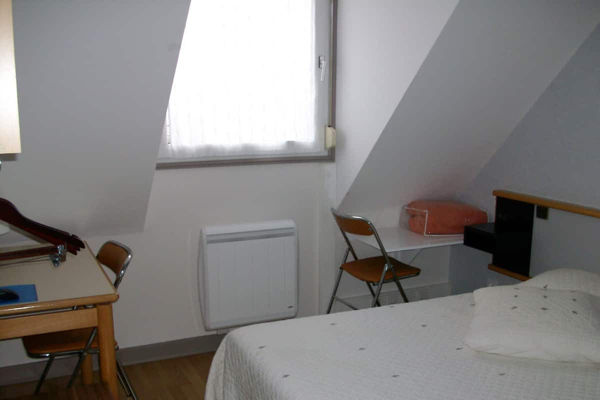 Una habitación pequeña y sencilla con cama, escritorio, silla y radiador.