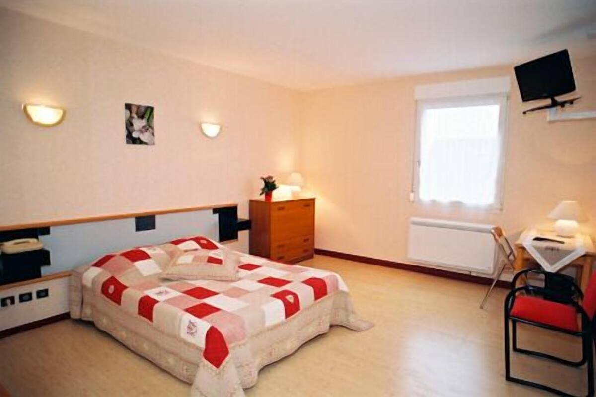Un dormitorio con cama, escritorio, silla, cómoda, televisor y ventana.