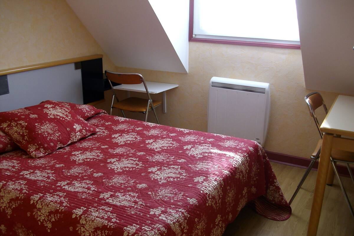 Un dormitorio con cama, dos sillas, escritorio y radiador.