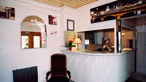 Una habitación con techo de madera curvada, una silla de madera oscura, una pared blanca con espejo y una pequeña mesa con lámpara.
