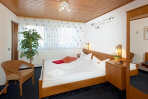 A hotel room with a wooden ceiling, a large bed with white bedding, a wooden nightstand, a wicker chair, a potted plant, and a wall with a motivational quote. - City Hotel Hanau (Hanau)
