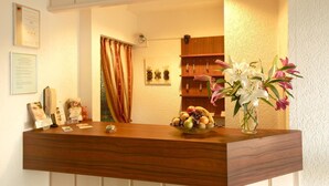 A reception desk with a wooden finish, a glass vase with flowers, and a fruit bowl.