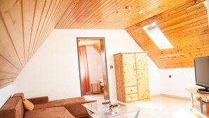 A modern loft-style room with a sloped ceiling, wooden beams, a glass coffee table, a brown sofa, a wooden wardrobe, and a television.