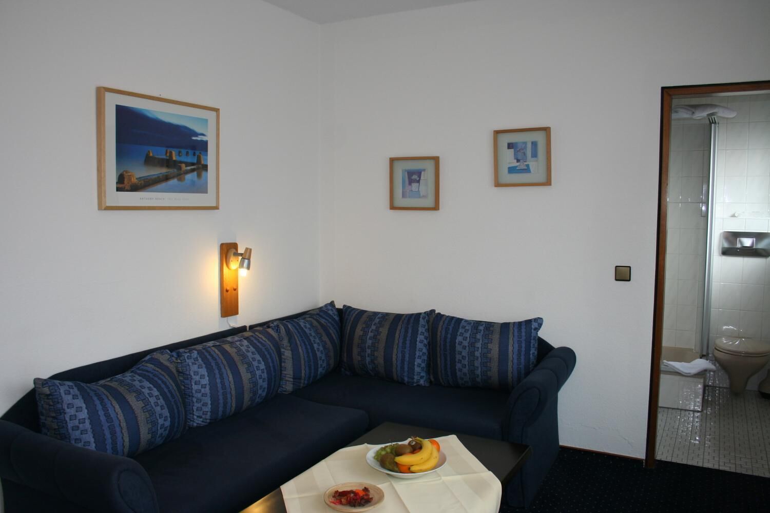 Ein Wohnzimmer mit einem dunkelblauen Sofa, einem kleinen Tisch mit Obst und zwei gerahmten Bildern an der Wand.
