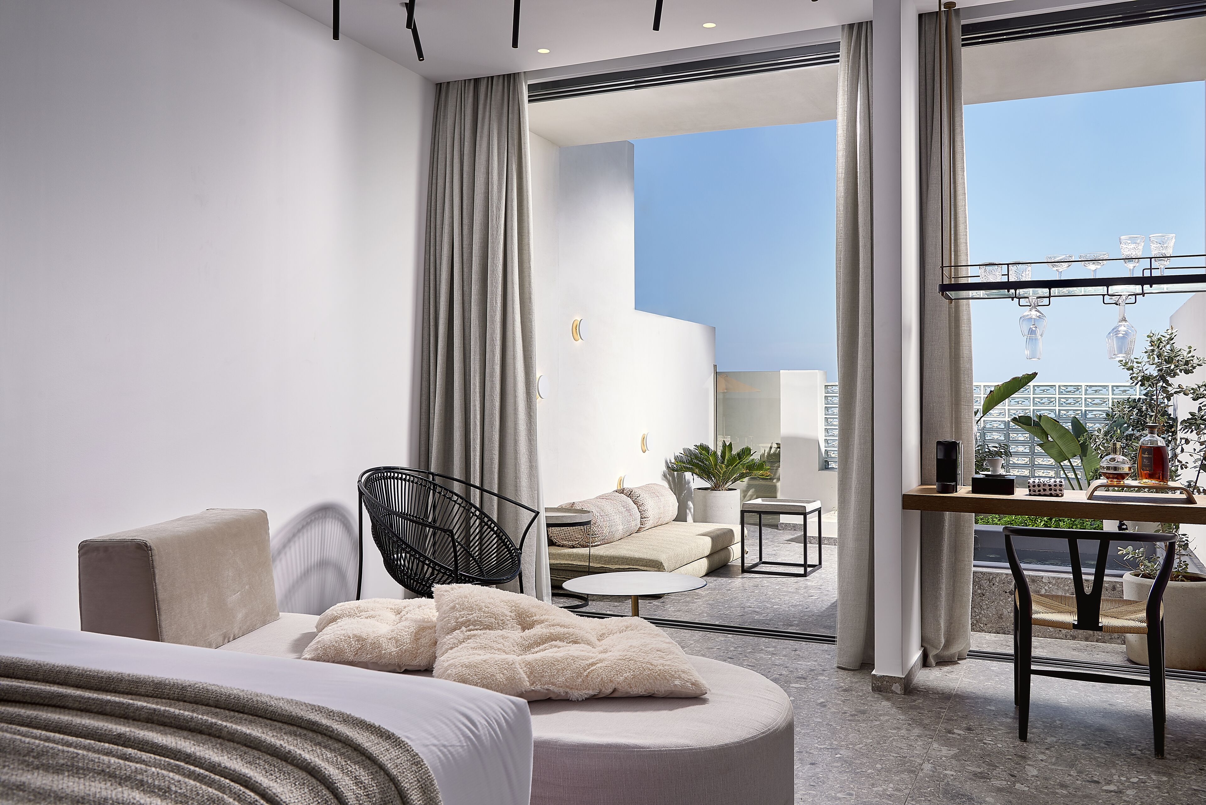 Et moderne hotelværelse med et stort vindue, en sofa, en lænestol, et lille bord og et skrivebord med en plante.