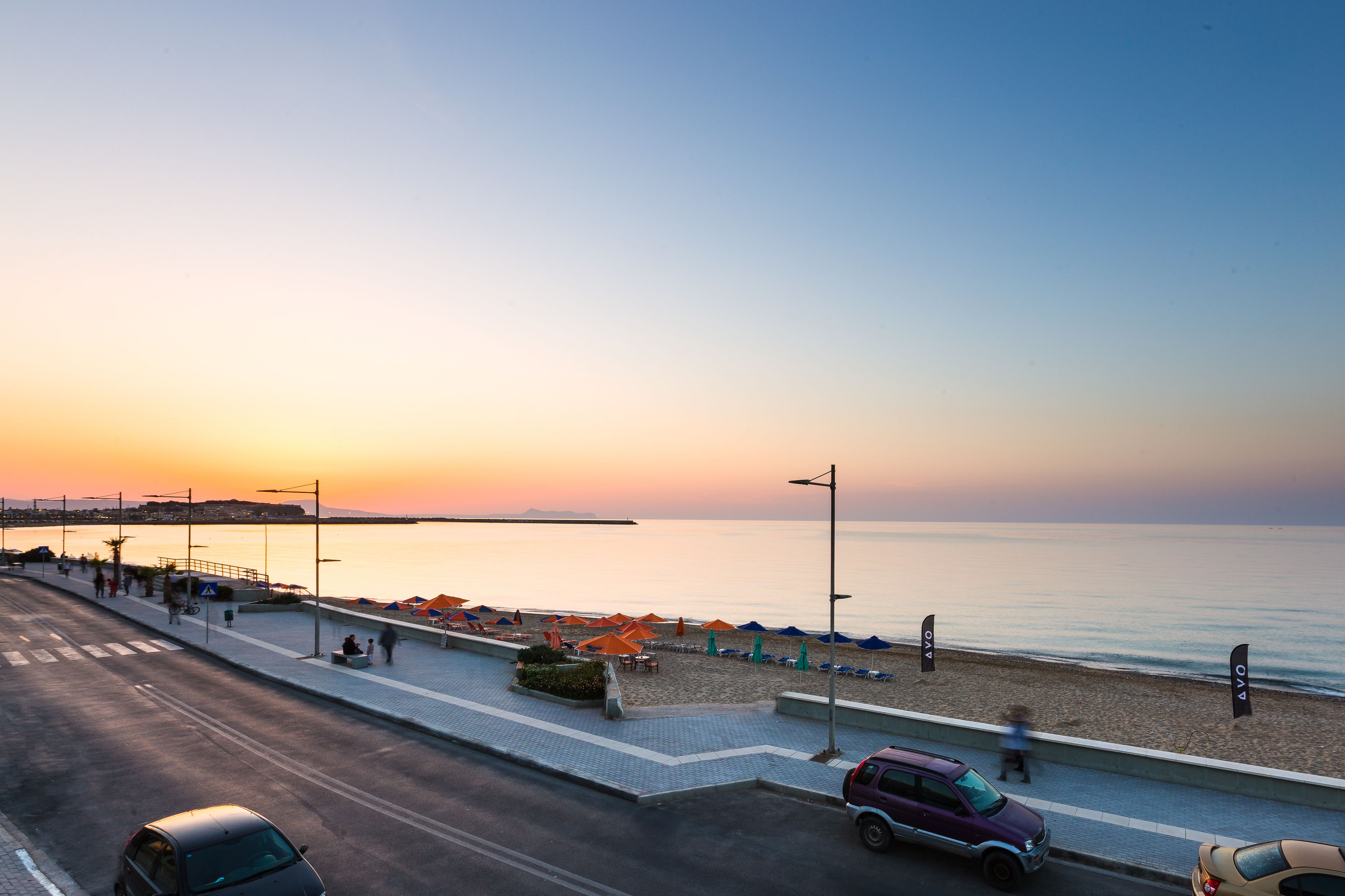 A coastal road with beachside seating and umbrellas, a pedestrian walkway, and a clear view of the sea.