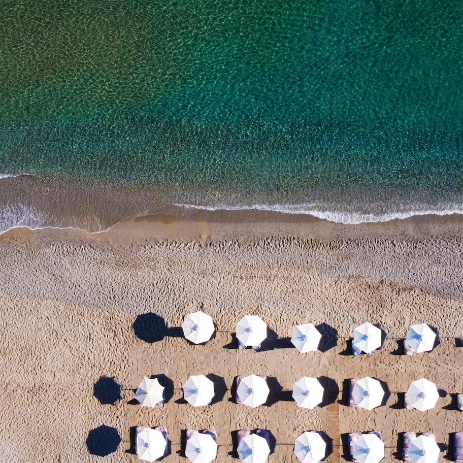 An aerial view of a beach with rows of umbrellas and lounge chairs, indicating a beach resort setting.