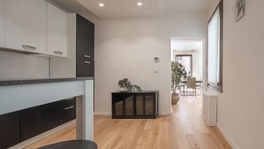 A modern kitchen with white and dark cabinets, a black countertop, and a wooden floor. There is a small black console table with a potted plant. - San Marco Prestige with Terrace by Wonderful Italy (Venice)