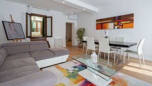 A modern living room with a sectional sofa, a glass coffee table, and a dining area with a black table and white chairs. - San Marco Prestige with Terrace by Wonderful Italy (Venice)
