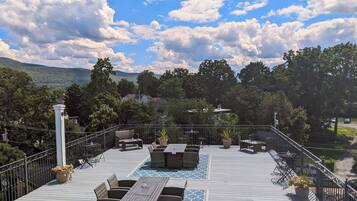 A deck with outdoor seating, surrounded by trees and a view of a hilly landscape.
