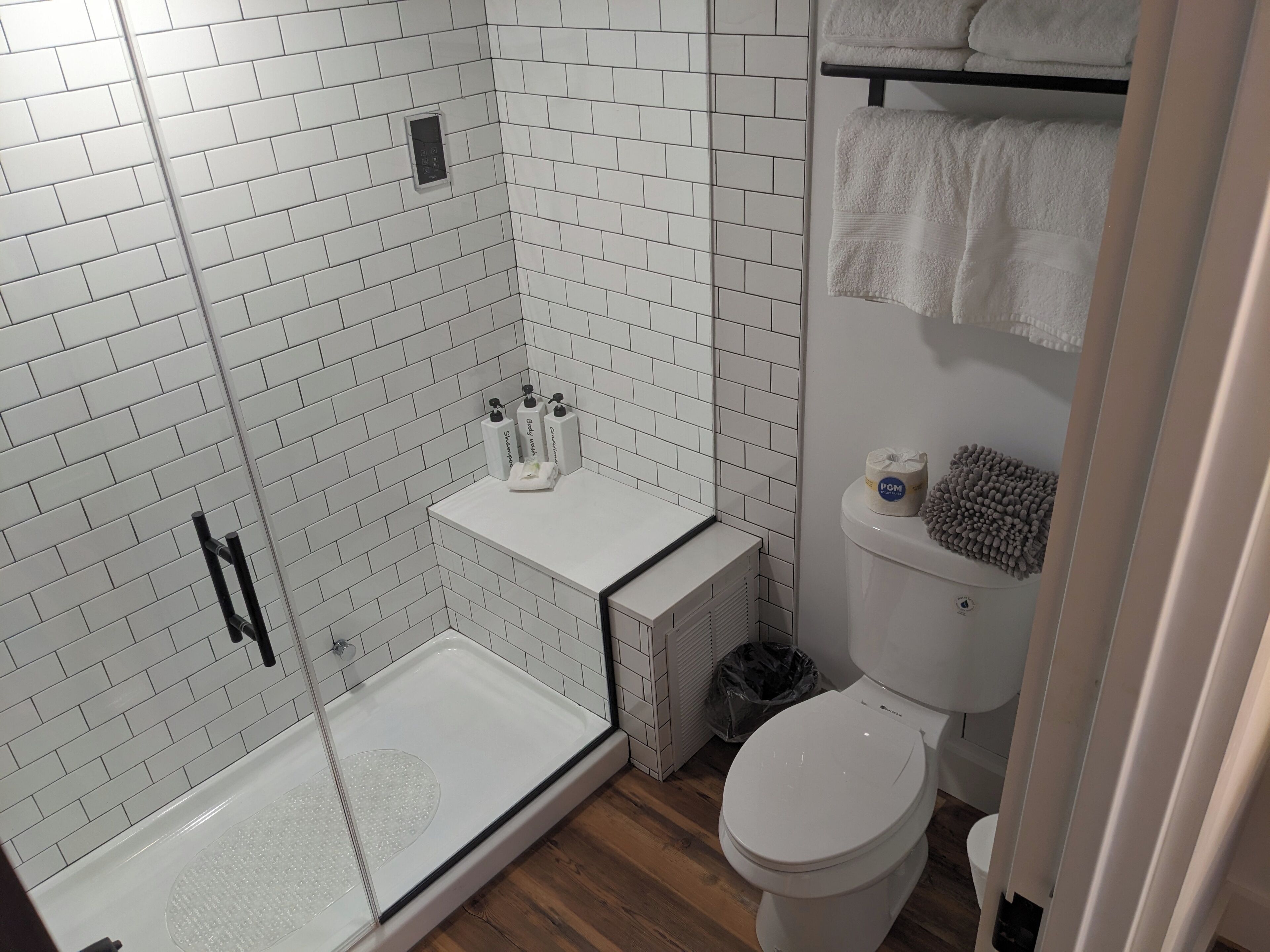 A modern bathroom with white subway tiles, a glass shower enclosure, a toilet, and a towel rack.
