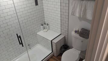 A modern bathroom with white subway tiles, a glass shower enclosure, a toilet, and a towel rack.