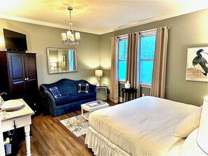 Una habitación de hotel con cama, sofá azul, escritorio con espejo, candelabro y ventana con cortinas.