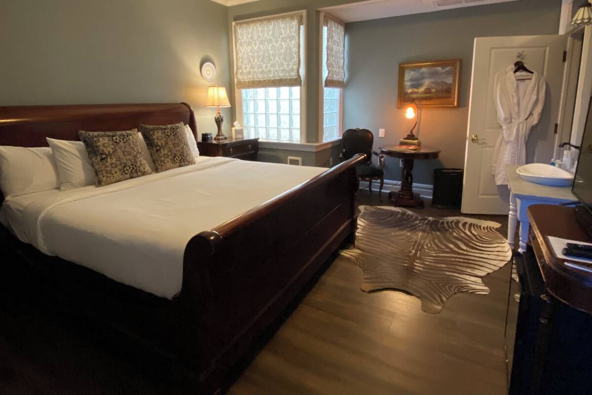 A bedroom with a large bed, a bedside table with a lamp, a window with curtains, and a robe hanging on the door.