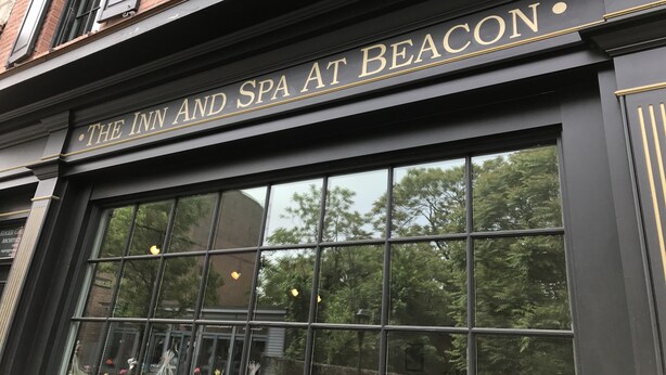The exterior of The Inn and Spa at Beacon, featuring a black facade with gold lettering and large windows reflecting trees and lights.