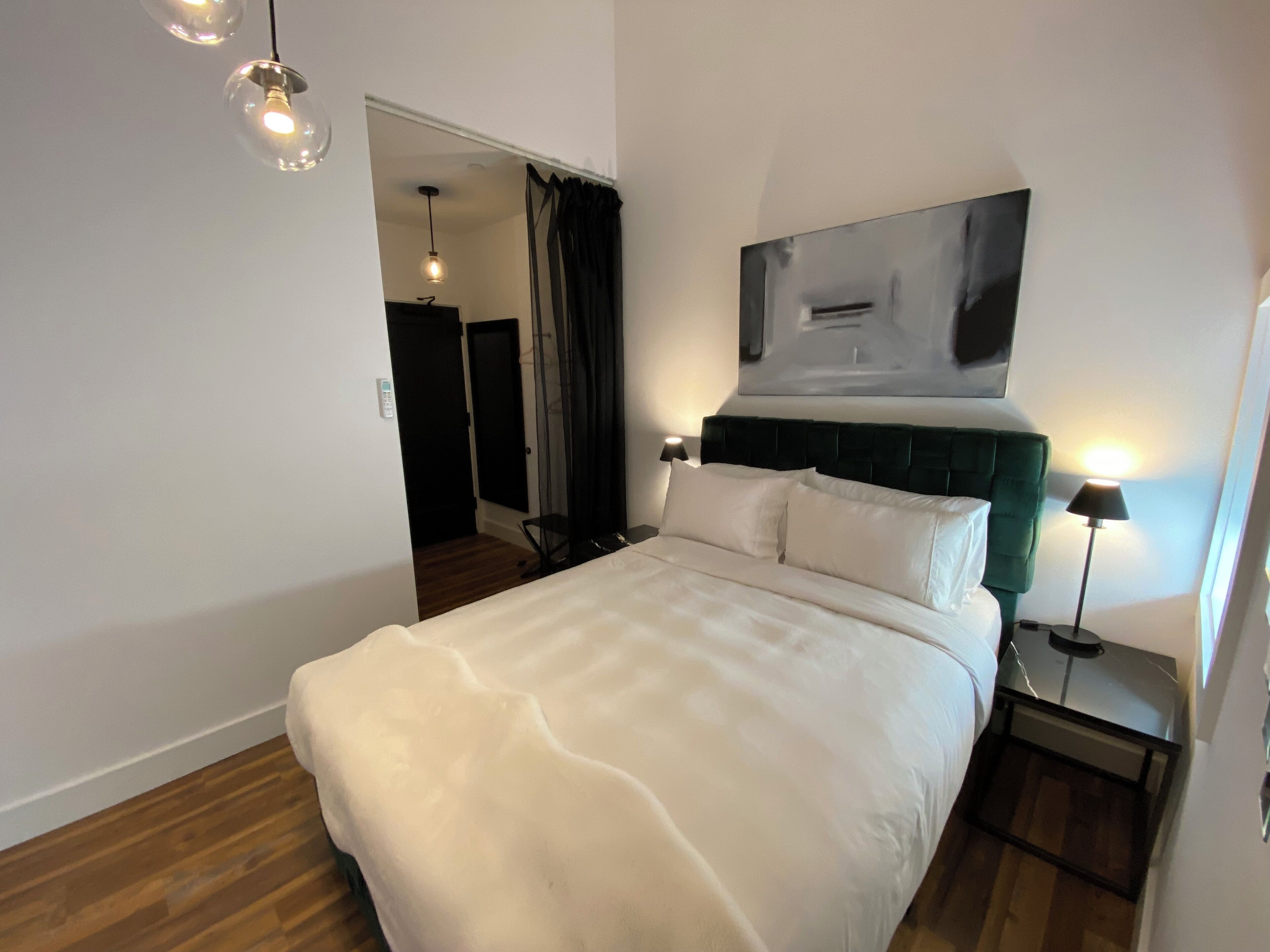 Ein modernes Hotelzimmer mit einem großen Bett, einem dunkelgrünen Kopfteil und einem minimalistischen Design.