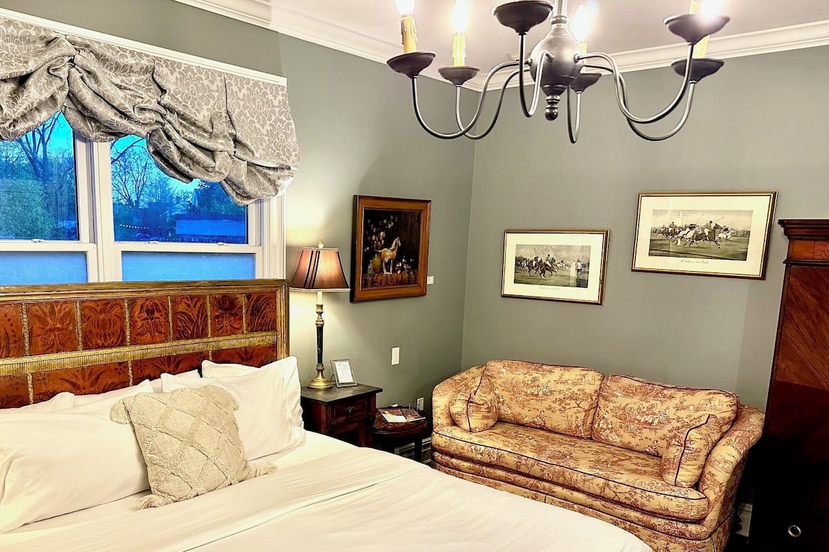 A bedroom with a large bed, a patterned sofa, and a chandelier.