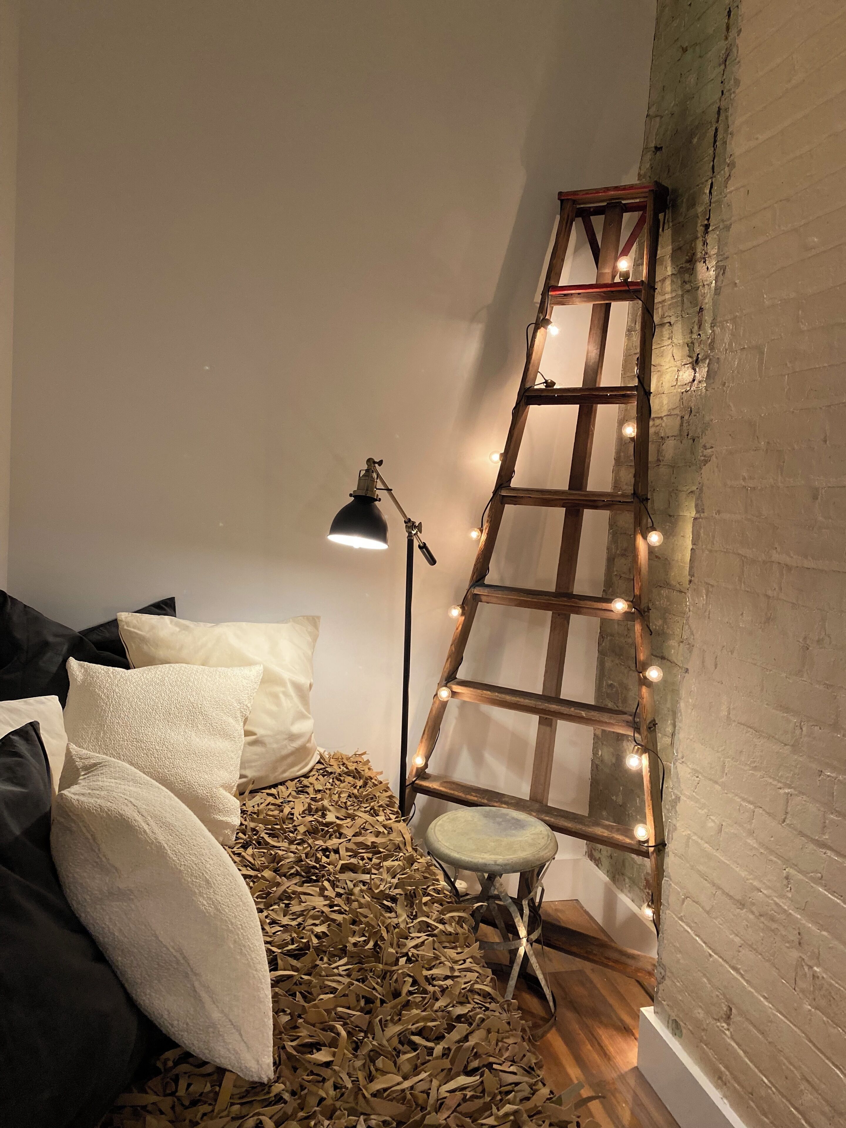 Un dormitorio con cama, almohadas, una escalera y luces colgantes.