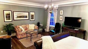 A hotel room with a bed, a sofa, a television, a chandelier, and framed pictures on the wall.