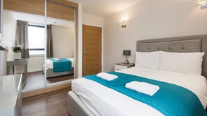 Un moderno cuarto de hotel con una cama grande, una mesita de noche con lámpara, un espejo, un armario y vistas a la ciudad a través del ventanal.